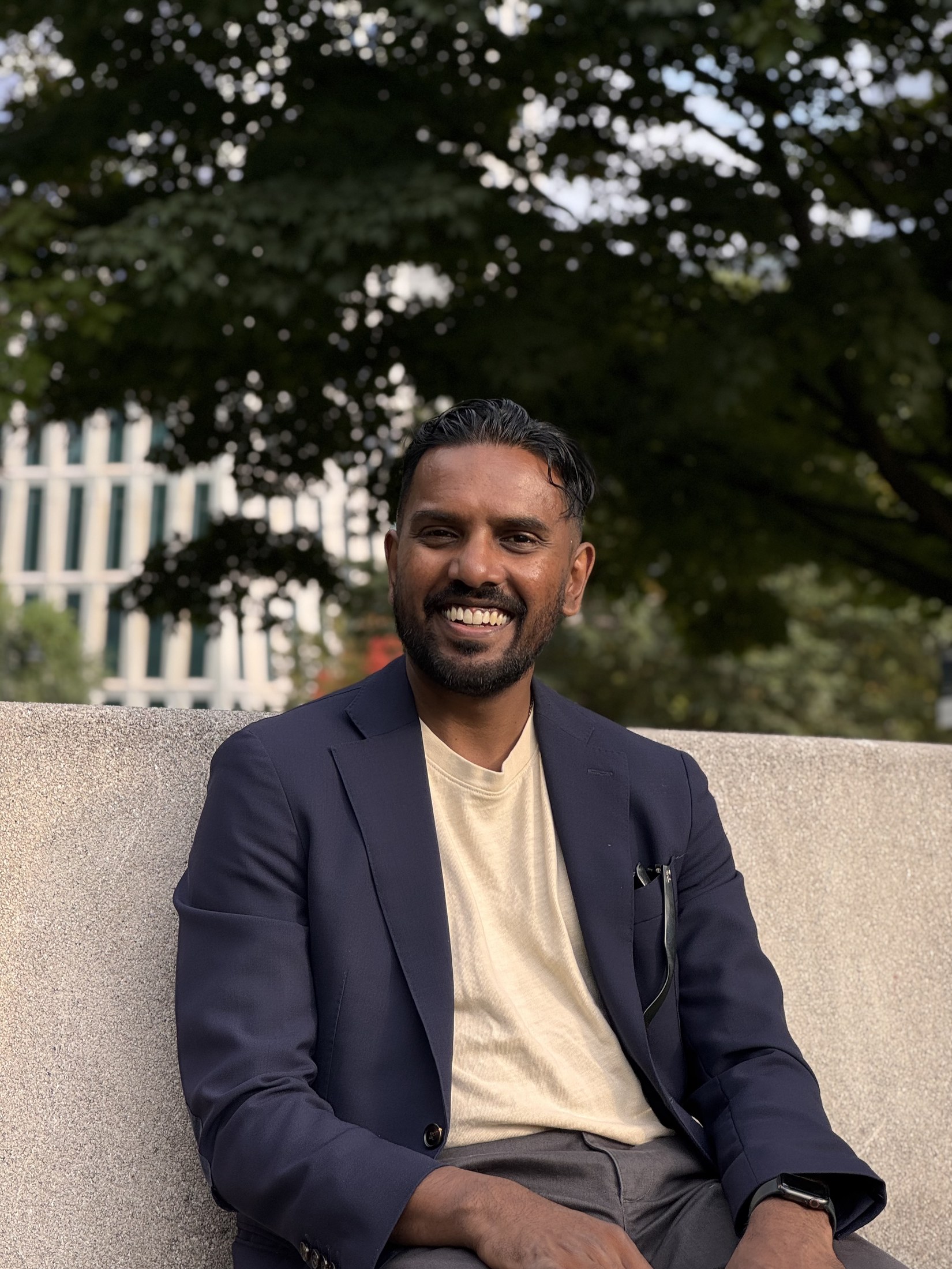 Christopher Balkaran smiling while seated outdoors on a stone bench
