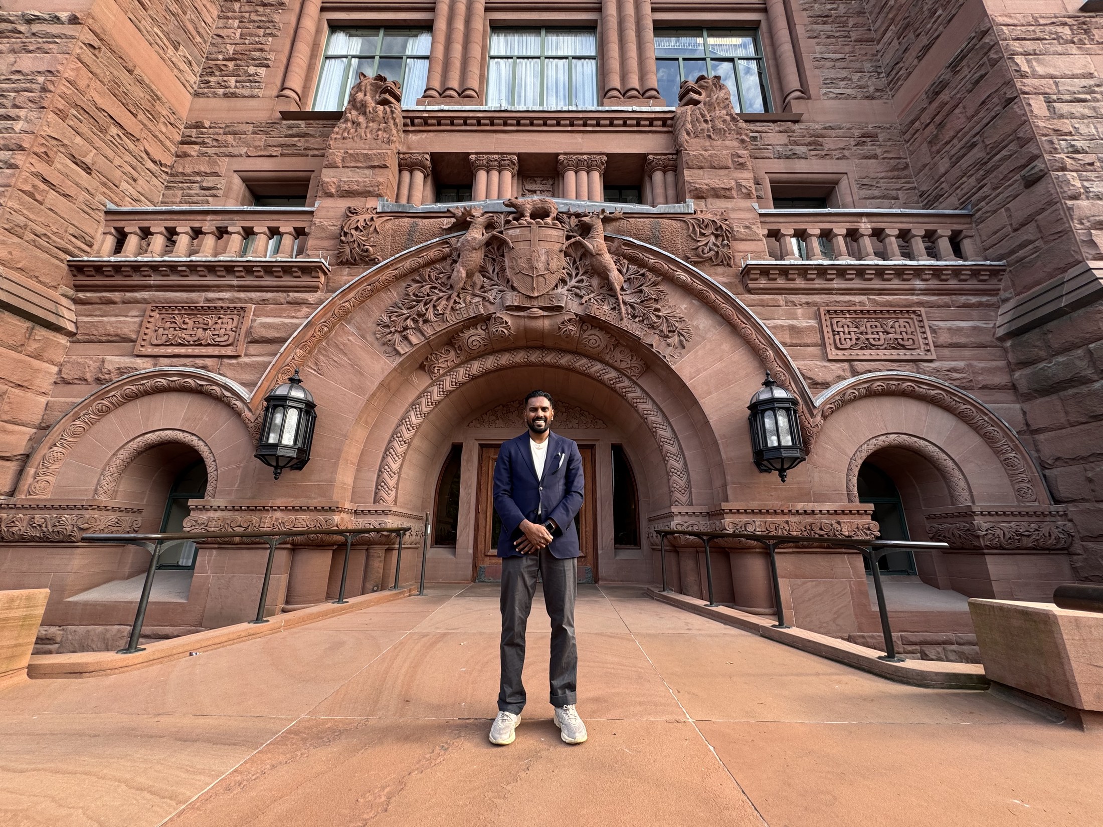 Christopher Balkaran standing beneath the entrance arch of the Ontario Legislative Building